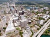 Aerial view of a city downtown area with numerous high-rise buildings, roads, and a nearby lake surrounded by greenery.