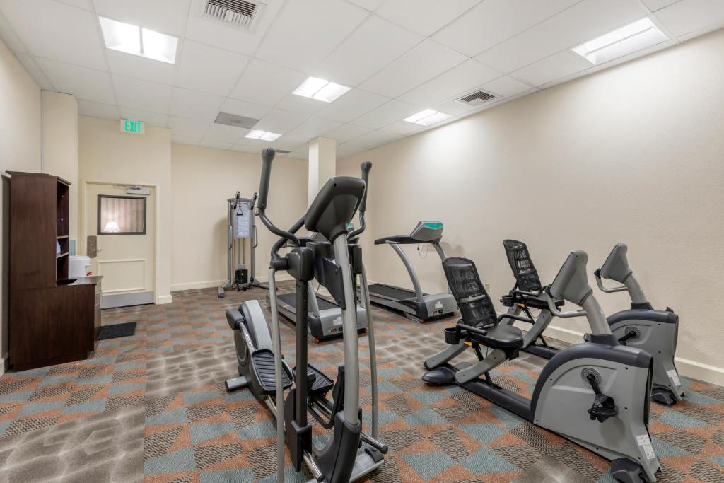 A gym with exercise equipment, including a treadmill, elliptical, and stationary bikes, in a room with fluorescent lighting and patterned carpet.