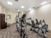 A gym with exercise equipment, including a treadmill, elliptical, and stationary bikes, in a room with fluorescent lighting and patterned carpet.