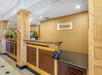 Hotel reception area with wooden counters, a Clarion Hotel sign on the wall, potted plants, and a tiled floor.