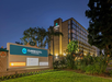 Clarion Hotel exterior at twilight with illuminated signage, a tall building structure, and surrounding trees.