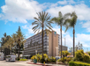 A modern hotel building with multiple floors is surrounded by palm trees on a sunny day.