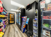 Small convenience store aisle with shelves of snacks, drinks in coolers, and a Red Bull fridge. Door labeled "Tundor Room." Light wood floor and black walls.