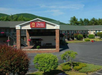 Hotel exterior with a red "Clarion Inn & Suites" sign, surrounded by trees and mountains, with a spacious parking lot in front.