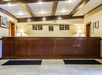 Hotel reception area with a wooden desk, framed pictures on the wall, and two lit lamps on each side. The ceiling features exposed wooden beams.