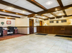 Hotel lobby with tiled floor, wooden beams on ceiling, and wood-paneled reception desk. Computer workstations are on the left, with framed art and certificates on the walls.