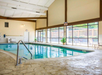 Indoor swimming pool with large windows, poolside chairs, and a textured stone floor.