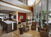 Hotel lobby with modern decor, featuring brown leather chairs, a central white counter, various plants, and large windows allowing natural light to fill the space.
