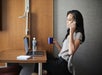 Guest chatting on the cellphone while holding a cup of coffee, with a laptop on top of a work desk inside a guest room.