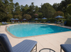 Outdoor swimming pool surrounded by lounge chairs, blue umbrellas, and trees.