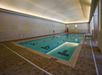 Indoor swimming pool with lane markers, beige tiled floor, and a high ceiling.
