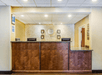 Hotel reception desk with a stone wall background, two computer monitors, and a small sign mounted on the wall. The area is well-lit, featuring a wooden countertop.