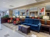 Hotel lobby with blue and red chairs, wall mirrors, framed sailboat paintings, and potted plants. Ceiling lights illuminate the space.