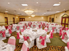 A banquet room with round tables with chairs around them, both covered in white cloth with pink bows around the chairs.
