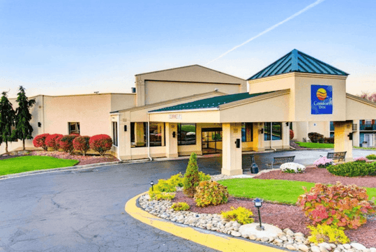 The front exterior entrance and covered driveway of the Comfort Inn Conference Center Pittsburgh with landscaping around it.