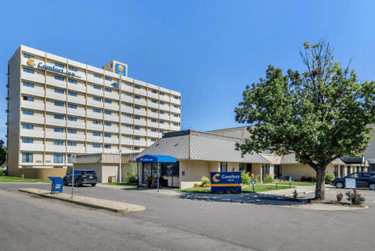 Wide shot of the exterior of the Comfort Inn Denver Central with a small tree in front of it on a bright and sunny day in Denver.