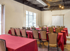 A meeting room with a few rows of red cloth covered tables with beige chairs lined up in front of a projector screen with a large window to the left of it.