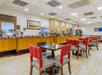 A dining room with brown tables with beige and red chairs and a full breakfast bar running the full length of the left wall.