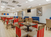 A dining room with brown tables with red and beige chairs and a few blue booth seats along the far all at the Comfort Inn Denver Central.
