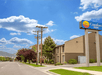 Street view of Comfort Inn with blue sky and clouds. Brown building, green trees, and power lines visible.