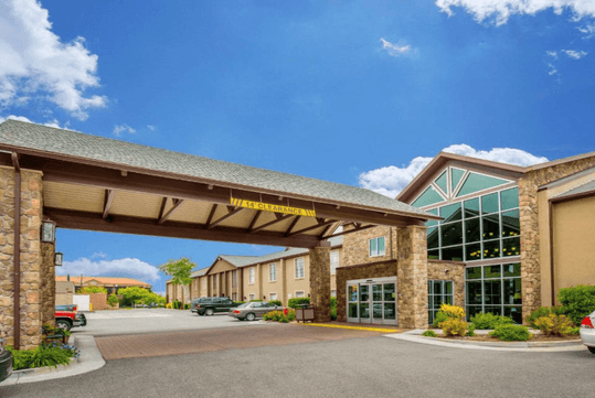 Exterior of a hotel with stone architecture and large windows, featuring a covered driveway labeled with a 14-foot clearance sign.