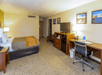 Hotel room with a bed, desk, chair, TV, and lamps. Wall art decorates the beige walls. The floor is carpeted, and the room has a warm, neutral color scheme.