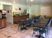 A small dining area with several tables and chairs, a drink dispenser, and a buffet counter against a pale green wall.