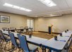 Conference room with U-shaped table arrangement, chairs, a podium, and mugs on the tables. A framed picture hangs on the wall.