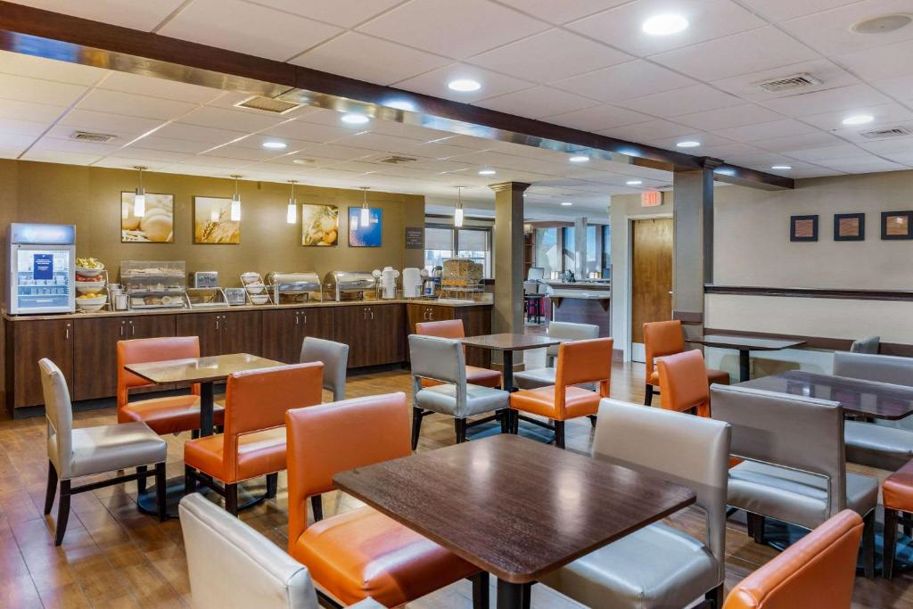 Hotel dining area with a variety of tables and chairs, breakfast buffet in the background, and ceiling lights illuminating the room.