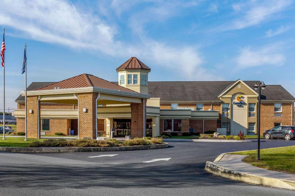 A two-story hotel building with a brick facade, a covered entrance, and flags displayed outside. A car is parked in the lot under a clear blue sky.