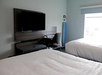 Hotel room with two double beds, a wall-mounted TV, a desk with a chair, and an ironing board by the window.