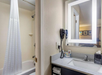 A well-lit vanity with fresh towels, hair dryer, complimentary toiletries and a tub inside a private bathroom.