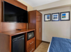 Work desk, flat-screen TV, microwave, mini-refrigerator, and a closet inside a guest room.