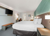 Hotel room with a double bed, white bedding, wall-mounted TV, desk, chair, nightstand, bench, and modern decor.