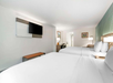 Hotel room with two neatly made double beds, a wall-mounted TV, a desk, and framed art. Room features soft lighting and neutral colors.