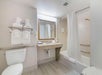Hotel bathroom with a toilet, vanity sink, and a shower-tub combo. White towels are neatly arranged on shelves and the bathtub, under bright lighting.