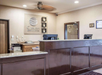 Hotel reception area with a granite counter, two computer monitors, and wooden accents. Wall features the "Comfort Inn & Suites" logo. Warm lighting and beige wall color create a welcoming atmosphere.