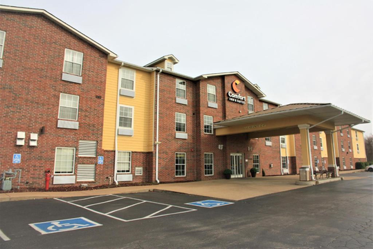 Exterior view of a brick and yellow hotel building with a covered entrance and accessible parking spaces.
