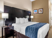Hotel room with a neatly made bed featuring white linens and a blue accent runner. Two bedside tables with lamps, and framed artwork on the brown wall above.