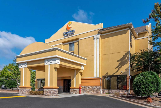 A yellow and beige hotel building with a sign reading "Comfort Inn & Suites" and an entrance canopy, set against a blue sky.