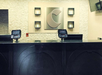 Hotel front desk with two check-in terminals and a large logo on the wall behind. Walls are textured with a light beige color.