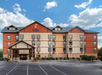 Four-story Comfort Inn hotel with a colorful exterior, featuring a front entrance and an empty parking lot, under a partially cloudy sky.