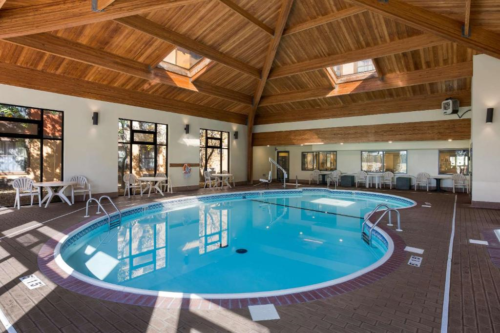 Indoor swimming pool with skylights, surrounded by lounge chairs and tables on a tiled deck, under a wooden ceiling.