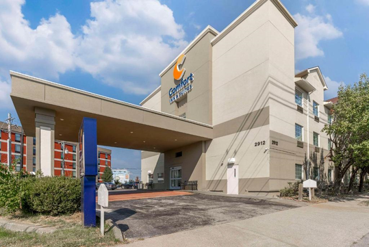 A beige Comfort Inn & Suites building with a porte-cochère and signage, under a partly cloudy sky.