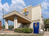 Exterior of a Comfort Inn & Suites hotel with a clear sky and a sign indicating the entrance. The building features a covered driveway and surrounding greenery.