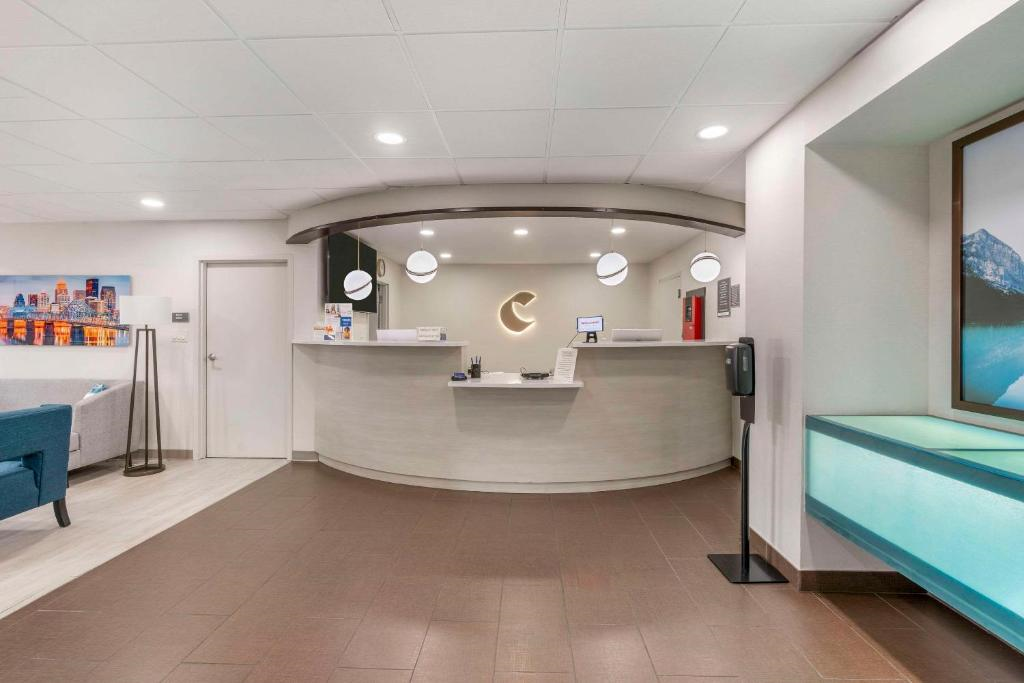 Hotel lobby with a curved reception desk, overhead lighting, and a sign featuring the letter "C." The area is decorated with a modern, minimalist design and artwork on the walls.