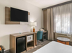 Hotel room with a bed, TV, desk, chair, microwave, mini-fridge, window with curtains, and a lamp.