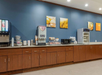 Breakfast buffet area with a coffee machine, juice dispenser, microwave, and cabinets. Wall art hangs above the counter.