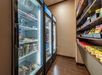 A room with two lit refrigerators stocked with frozen goods on the left and shelves filled with snacks on the right.