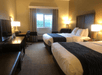 A hotel room with two queen beds, side table with lamp, accent chair, desk, and dress with a flat screen TV on it.